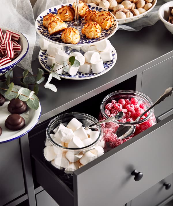 Siva komoda s velikim staklenkama i tanjurima ispunjenim kolačićima i slatkišima na gornjoj površini i u ladicama.