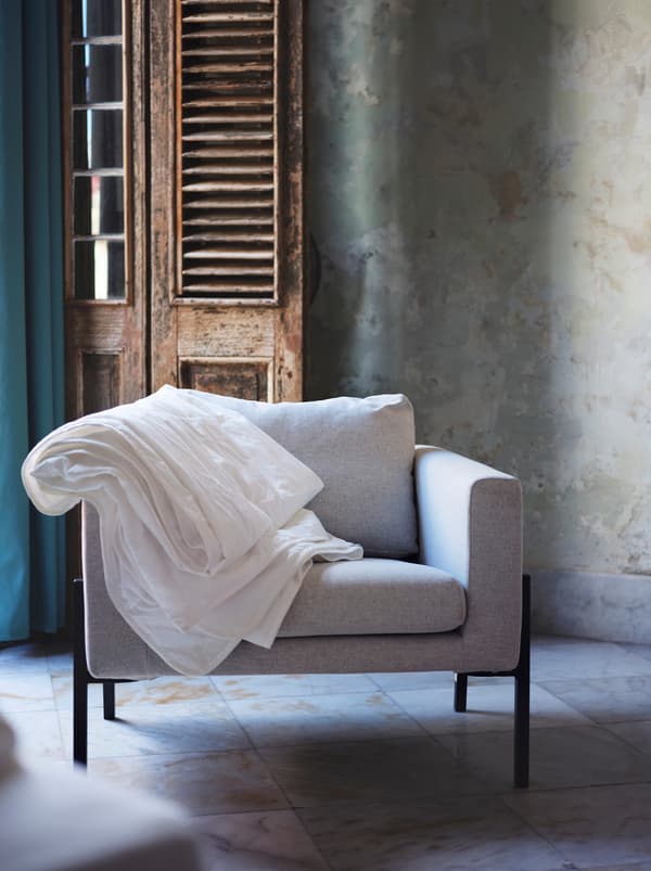 Sivá stolička s bielym paplónom preveseným cez opierku pri drevených dverách vo vidieckom štýle.