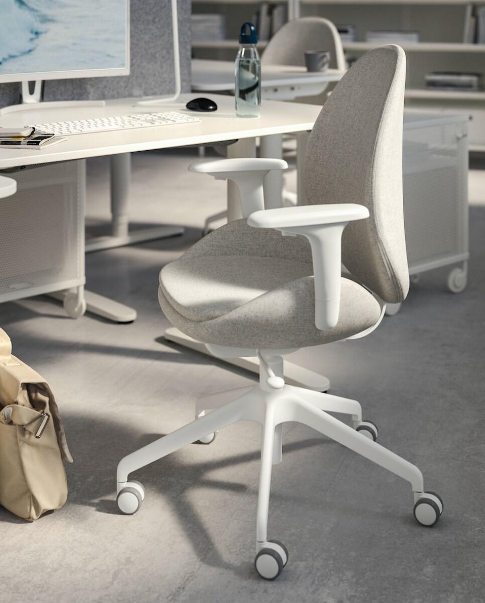 Siva uredska stolica s naslonima za ruke i kotačićima ispred bijelog stola s računalom u modernom uredu.