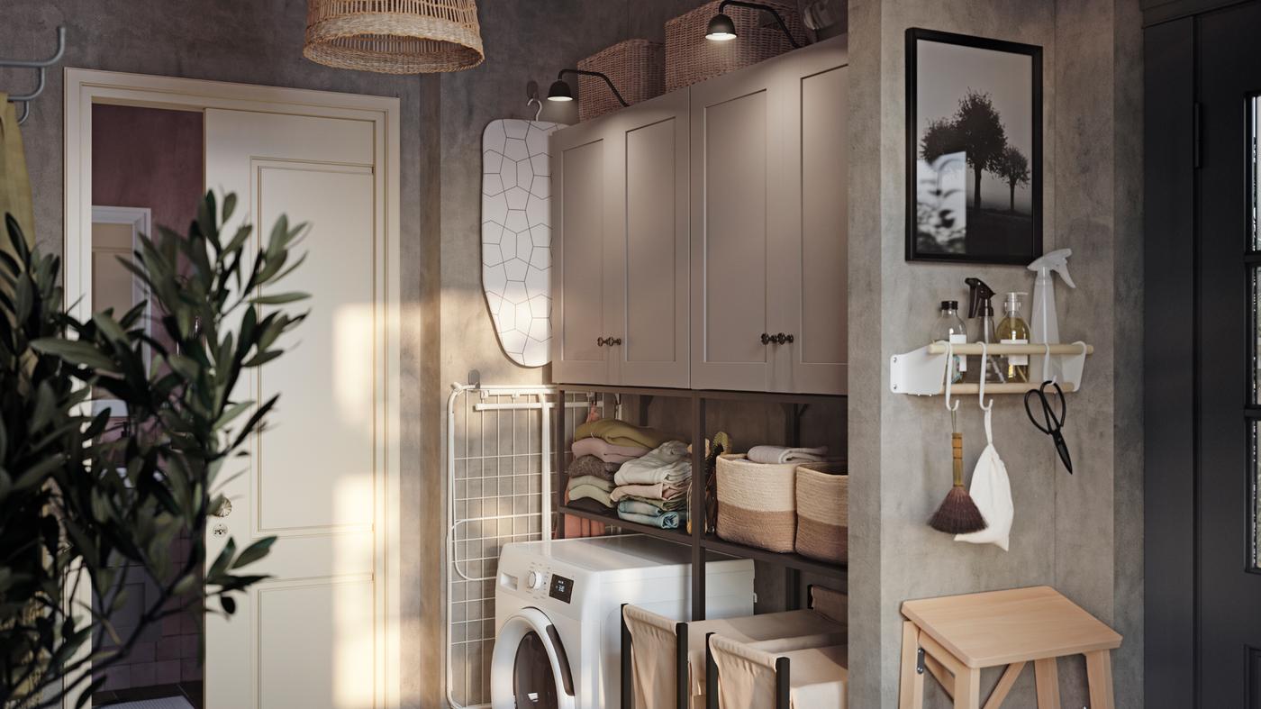 Siva vešernica s belim vratima ka kupatilu u pozadini, sivim ENHET ormarićima i belom veš-mašinom.