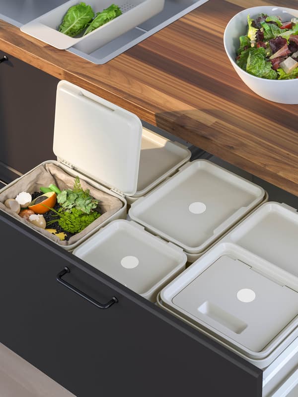 Sivé koše na triedený odpad HÅLLBAR v zásuvke čiernej kuchynskej skrinky.