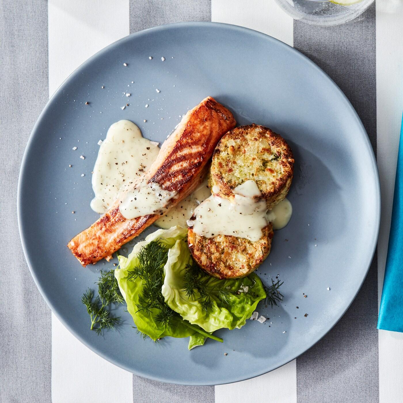 Sivoplavi tanjir sa SJÖRAPPORT fileom od lososa sa salatom, umakom, GRÖNSAKSKAKA medaljonima od povrća i DRAGON priborom za jelo.