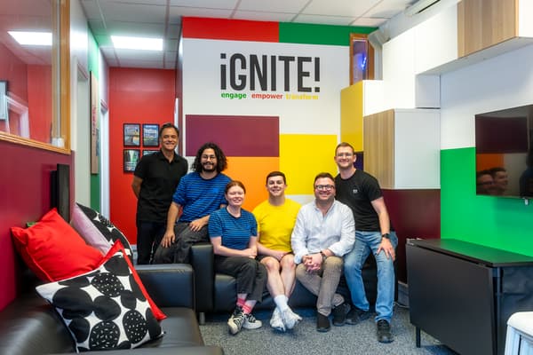 Siw people sitting on a black sofa in a room with multi-coloured walls. They are looking at the camera.