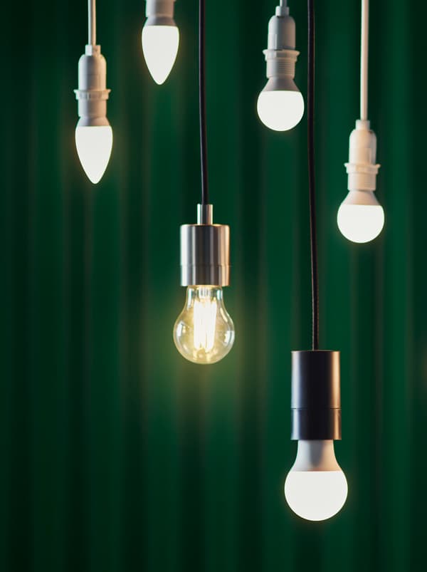 Six différents modèles d’ampoules LED de différents designs, suspendues à différentes hauteurs devant un rideau vert foncé.