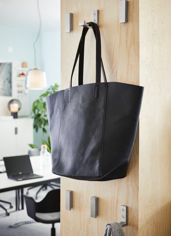 Six IKEA BJÄRNUM aluminium folding hooks mounted to a freestanding bookshelf, with a black tote hanging on one hook.