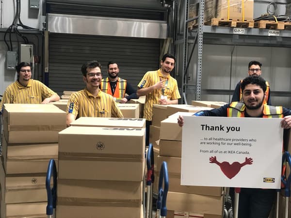 Six IKEA employees bearing carts filled with cardboard boxes, with one employee holding a 'Thank you' sign.