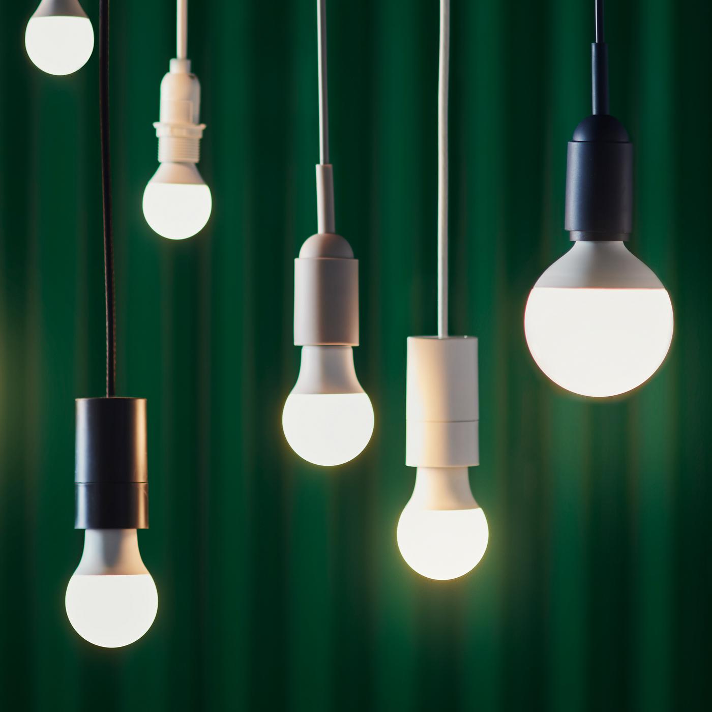 Six LED bulbs in various designs hung at different heights against the backdrop of a dark green curtain.