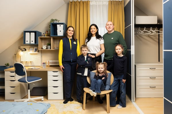 Six persons stand together in a renovated children’s room after a makeover.Two adults and three children pose in the finished space, featuring coordinated furniture, storage, and a study area, while an IKEA designer stands to the left.