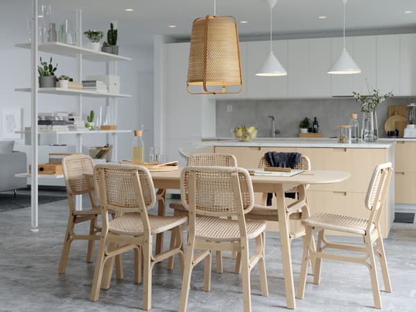 Six VOXLÖV chairs in light bamboo are standing around a large table with a big KNIXHULT pendant lamp in bamboo above it.