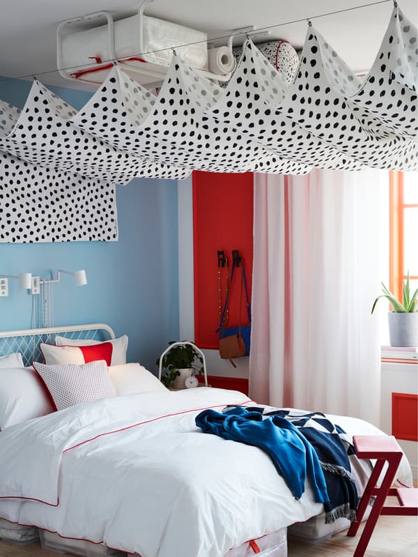 SKÄGGÖRT fabric hung between two curtain wires, hiding several MULIG clothes bars mounted onto the ceiling in a bedroom.