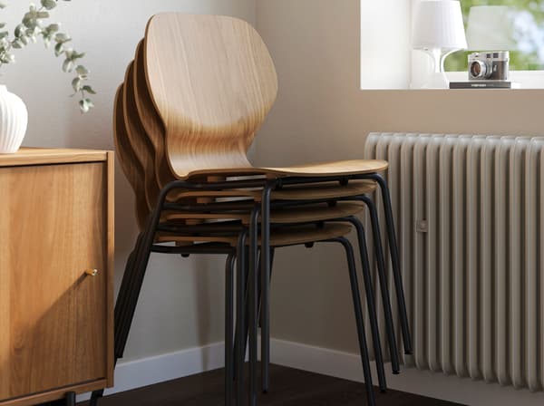 SKÅLSTA-tuoleja päällekkäin pinottuna huoneen nurkassa. Tuoleissa on pähkinäpuuviiluiset istuinosat.