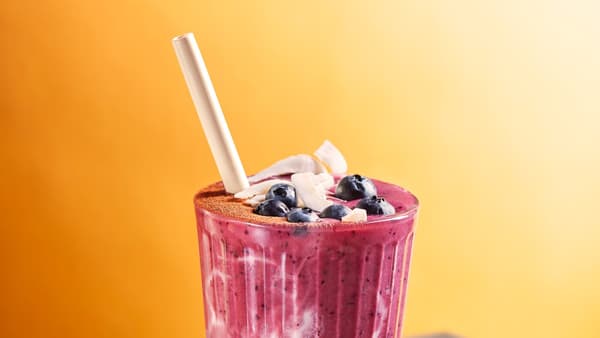 Sklenice smoothie  z červené řepy a ovesného mléka s bílou slámkou, na vrchu borůvky a kousky kokosu.
