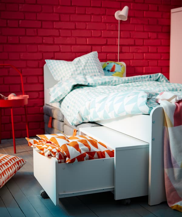 SLÄKT white bed and kid’s storage unit set up to store extra pillows and sheets underneath the bed