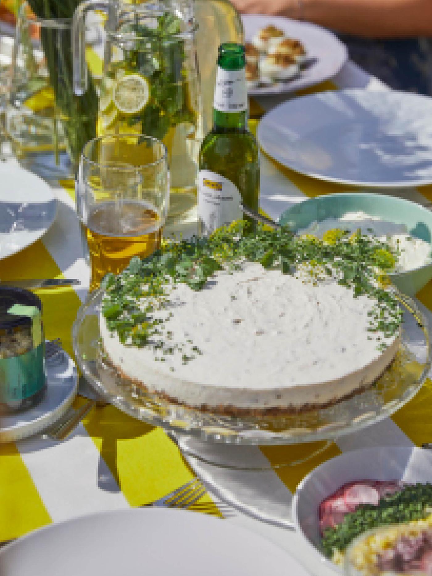Sleďový dort ozdobený pažitkou na stojanu ARV BRÖLLOP mezi dalšími lahůdkami na letně prostřeném stole.