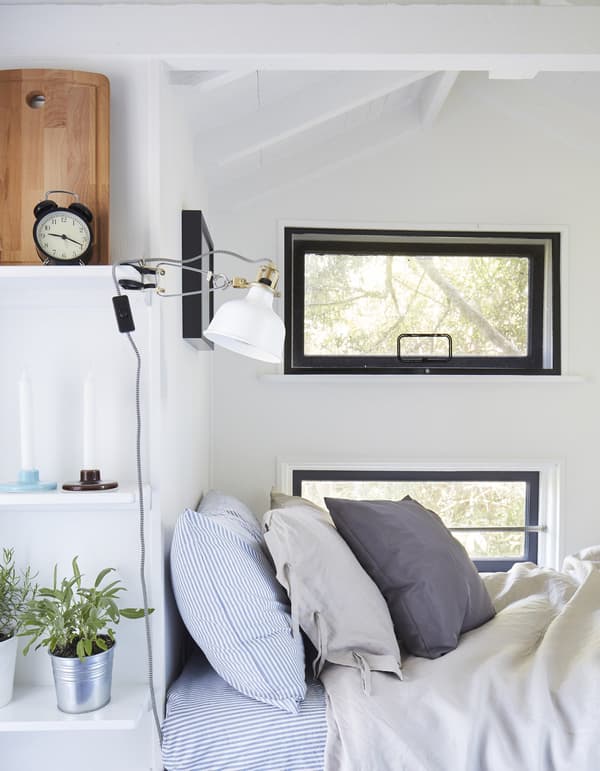 Sleeping area with cushions in grey and striped blue and white shown with a white clamp spotlight attached to a shelf.