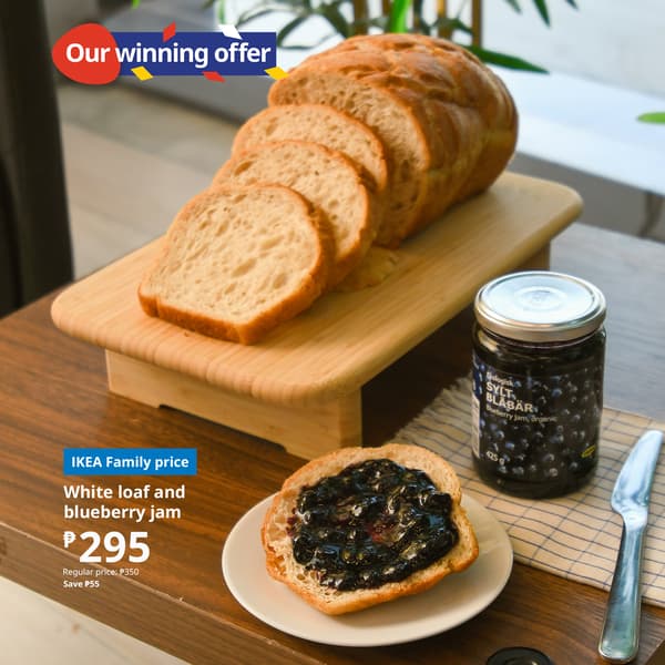 Sliced bread on a wooden board with a jar of blueberry jam beside it. A slice covered with jam is on a plate. Text highlights a special offer.