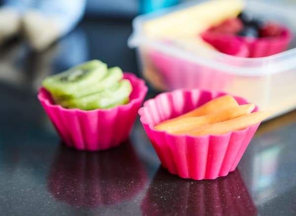 Sliced kiwi fruit and melon in two pink silicon muffin cups.