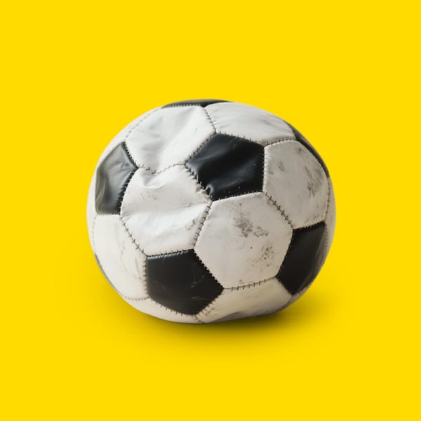 Sliten svartvit fotboll som är platt, placerad mot gul bakgrund.