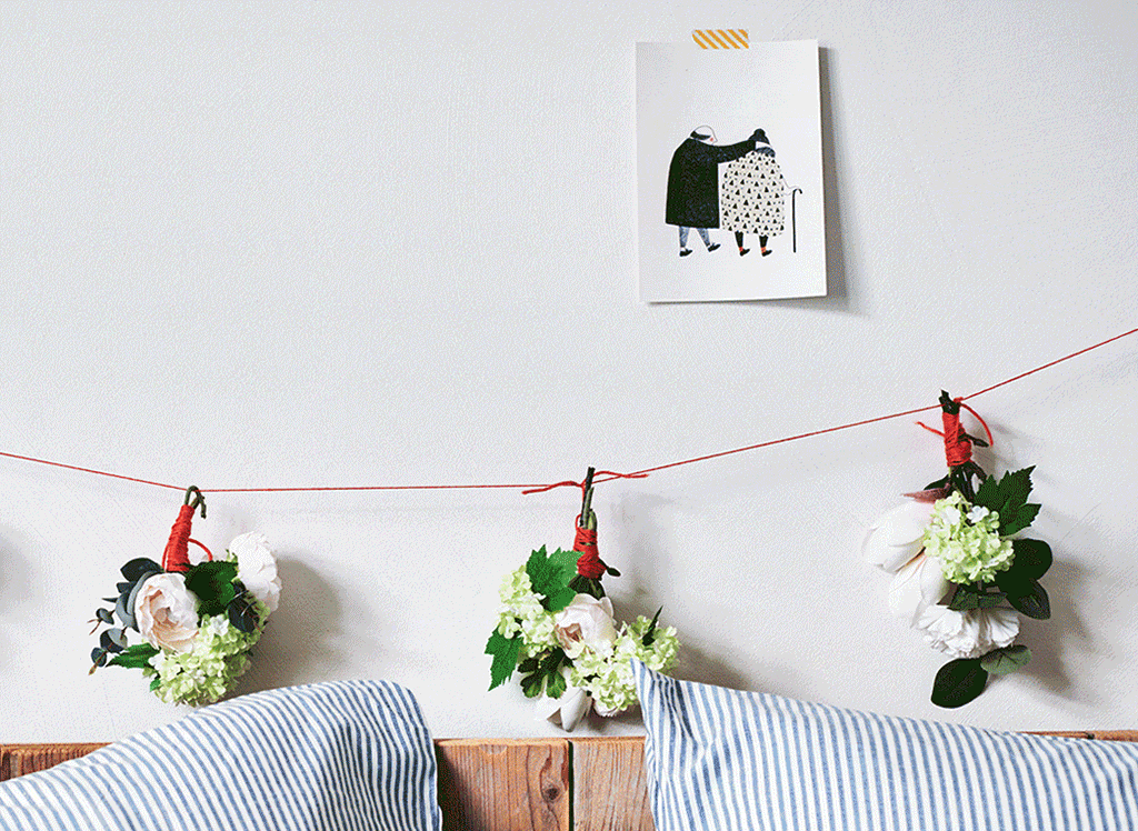 Small bouquets of flowers hanging on a line of string above a bed.