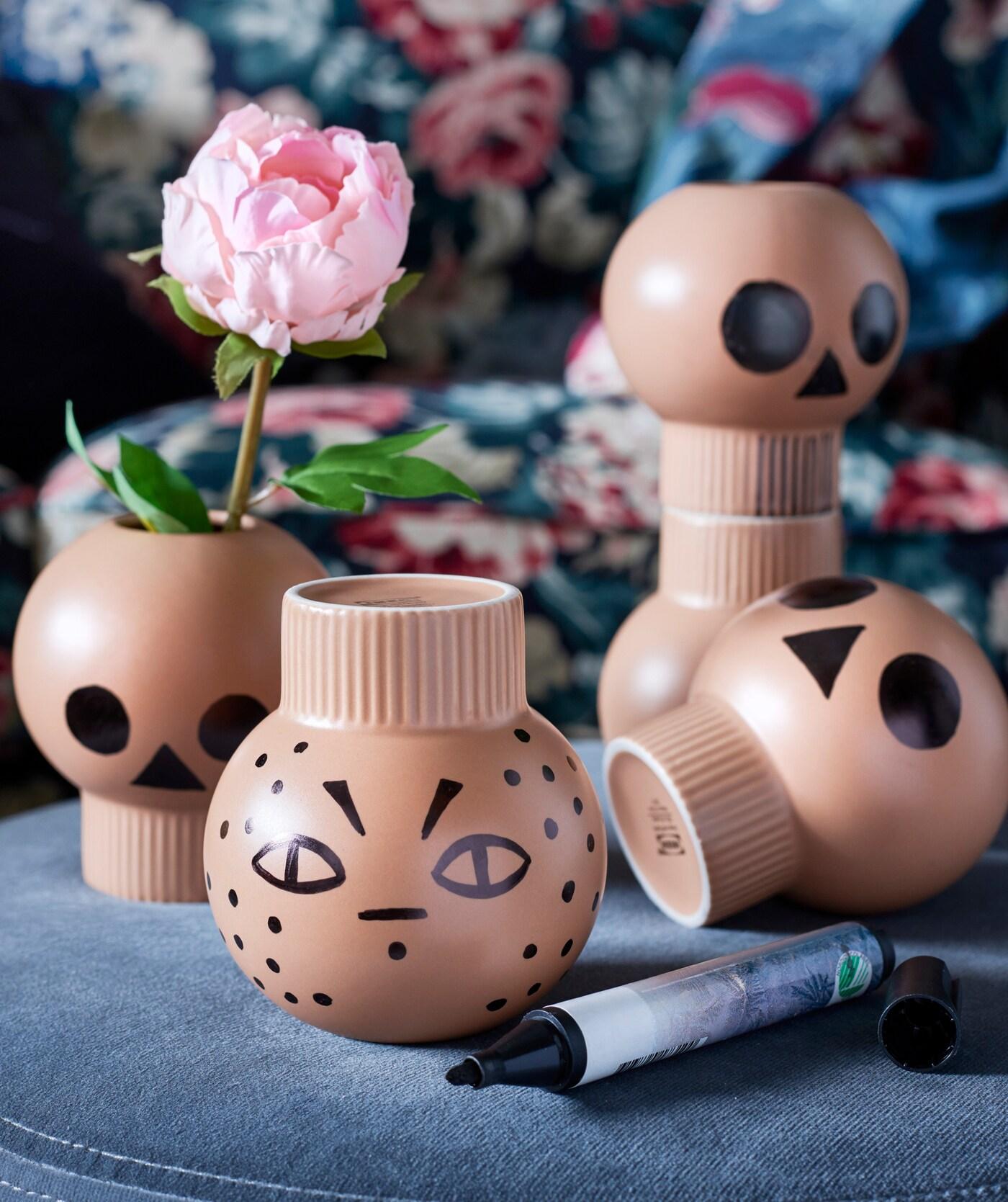 Small brown vases decorated with Halloween themed faces displayed with an artificial flower.