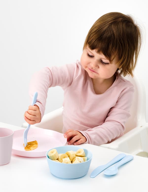 Small girl sitting in a highchair with sliced fruit with blue KALAS tableware.
