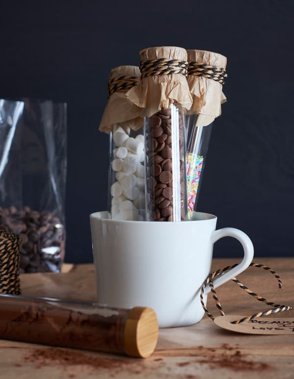 Small glass vials filled with toppings for hot cocoa and placed in a white mug.