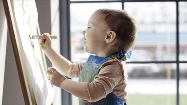 Small kid holding painting brush and expressing creativity on painting board
