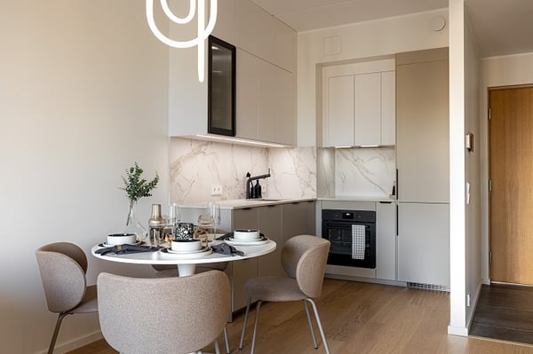 Small modern kitchen with marble backsplash, dining table, and beige cabinets.