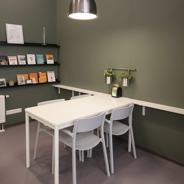 Small office meeting corner with white table, three chairs, green accent wall, and wall-mounted shelves with books.