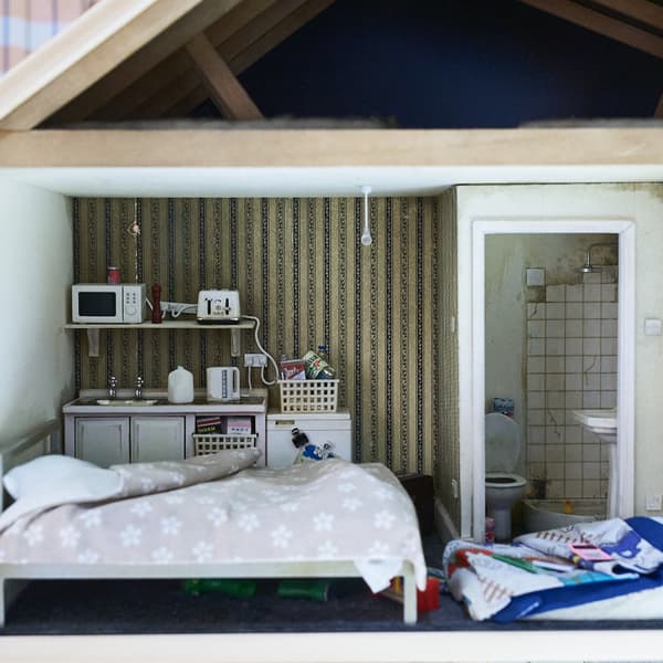 Small room with a bed plus a mattress on the floow. In the background a small kitchenette.