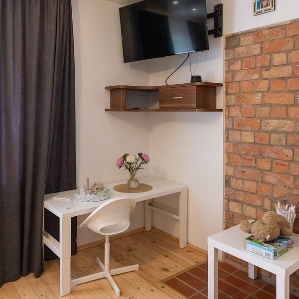 Small study corner with white desk, chair, wall-mounted TV, and brick accent wall