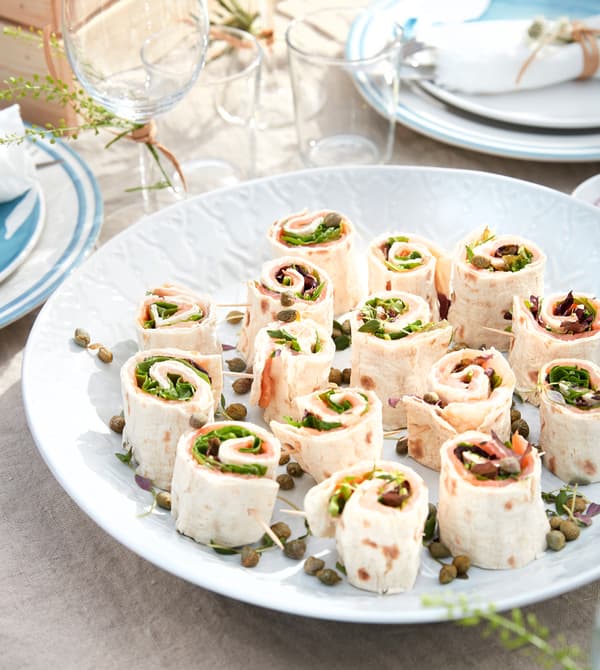Small wrap sandwiches are served on a white platter.