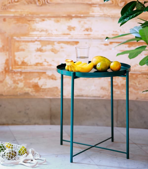 Smaragdovo zelený stôl s podnosom, na ktorom sú položené banány a rozličné citrusové ovocie.