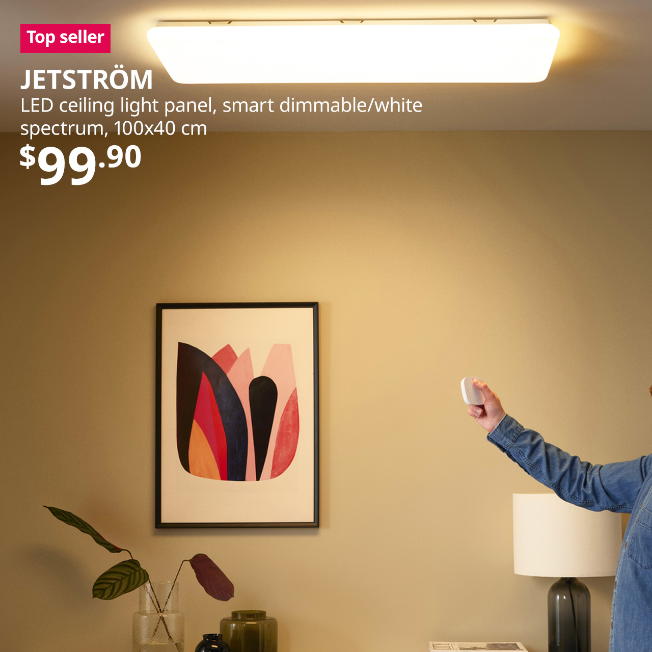 Smart LED ceiling light panel JETSTRÖM, dimmable, mounted on living room wall. Man holding smart remote points at ceiling light panel.