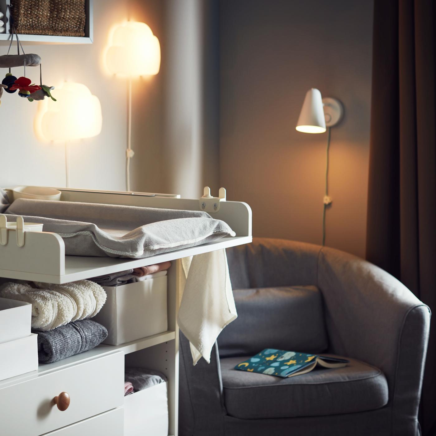 SMÅSTAD commode met dozen en opgevouwen spullen op de plank naast een middengrijze TULLSTA fauteuil in de hoek van een ruimte.