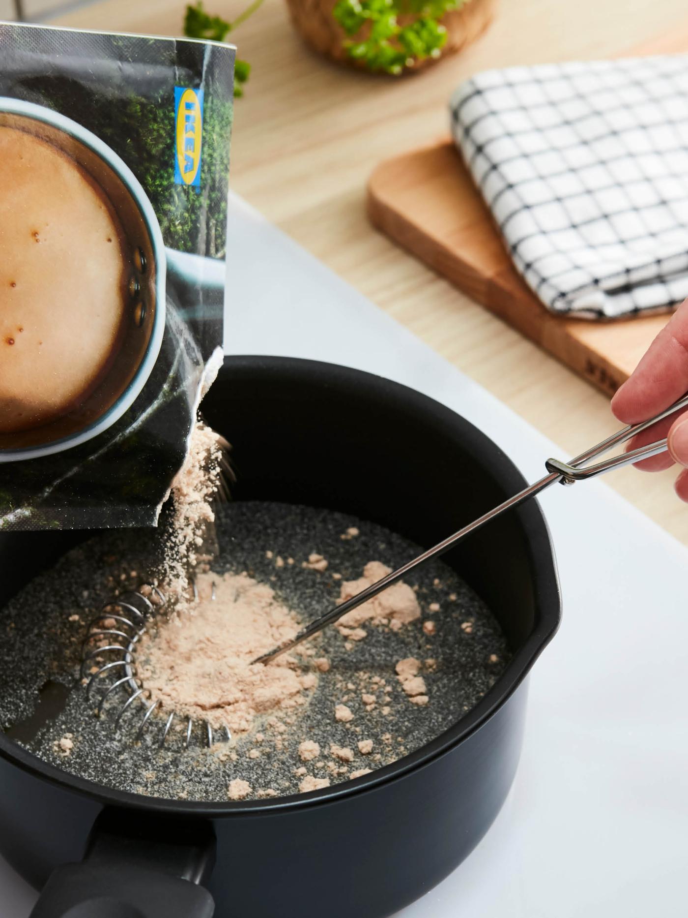 Směs na smetanovou omáčku ALLEMANSRÄTTEN se sype ze sáčku do vody v černém rendlíku.