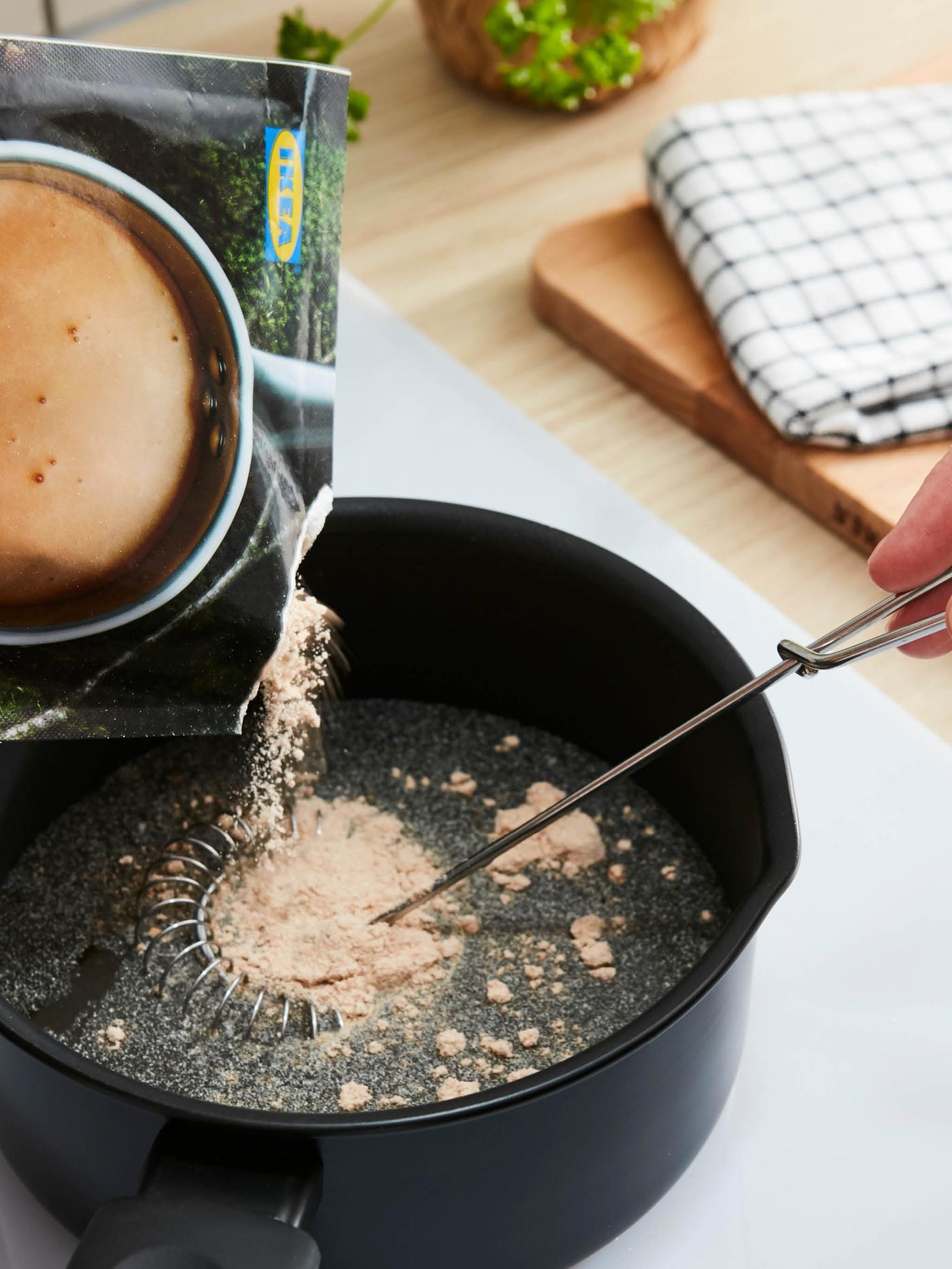 Směs na smetanovou omáčku ALLEMANSRÄTTEN se sype ze sáčku do vody v černém rendlíku.