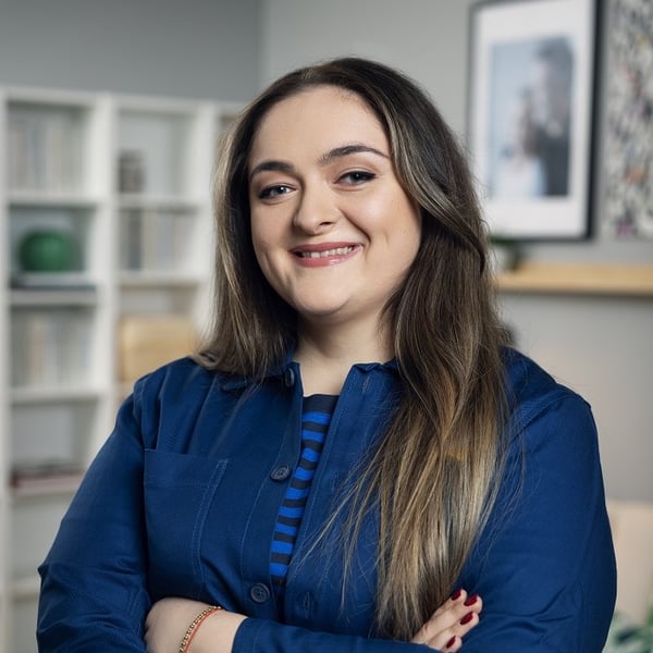 Smiling woman posing in modern living room with bookshelf and framed photos.