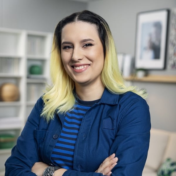 Smiling woman with blonde ombré hair in blue outfit standing in a modern living room.