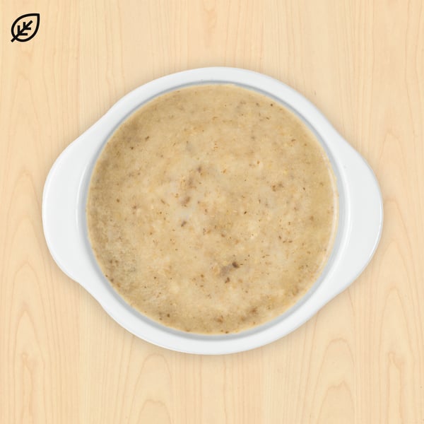 Smooth beige flatbread with visible grains on a white ceramic plate, set against a light wooden background. A leaf icon is in the top left corner.