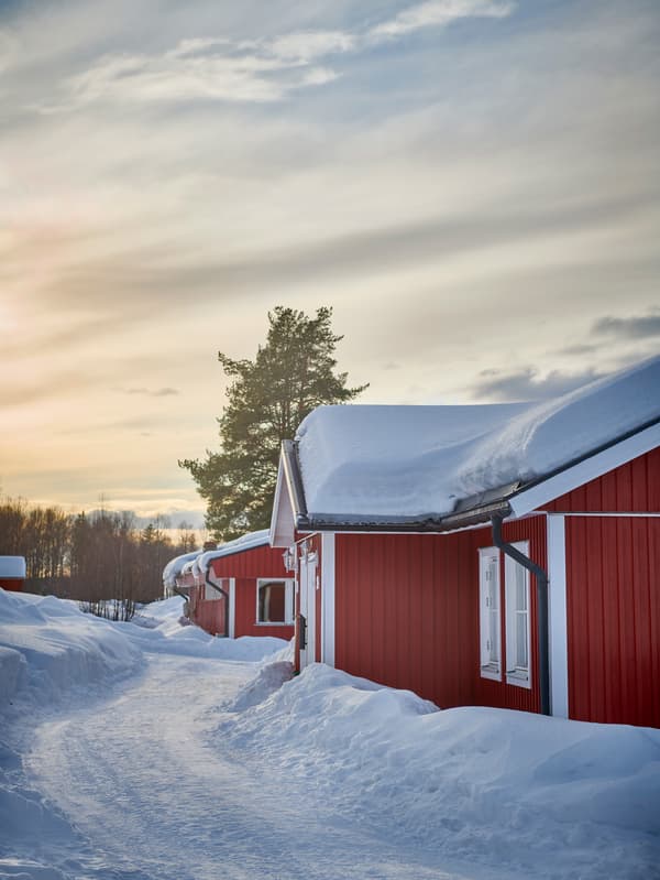 Snötäckt vinterlandskap med röda hus under en molnig himmel vid soluppgång eller solnedgång.