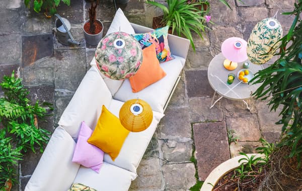 Sofa berwarna putih di patio batu semula jadi. Kusyen di atas sofa dan lampu pendan tergantung di atasnya, semuanya berwarna terang dan bercorak.