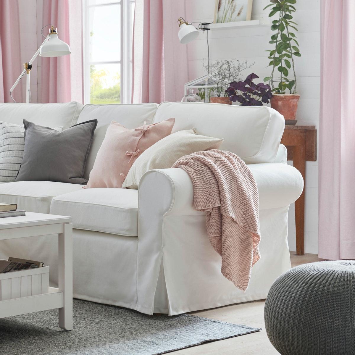 Sofá blanco EKTORP con cojines de colores y una manta rosada en el apoyabrazos.