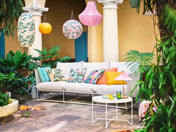 Sofá branco nun patio de pedra natural. Os coxíns no sofá e as lámpadas colgantes enriba presentan cores e padróns brillantes.