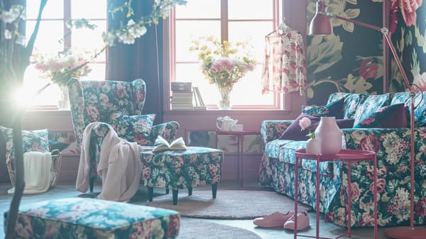 Sofa corak bunga yang padat, kerusi berlengan, bangku kaki dan kusyen di ruang tamu dengan kertas hias dinding bercorak bunga padat.
