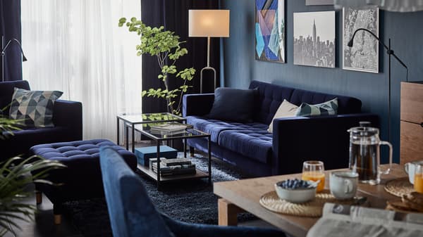 Sofa dan bangku kaki LANDSKRONA berwarna biru di sekeliling dua meja sisi kaca dengan gambar pada dinding di belakang dan tumbuhan di sebelahnya.