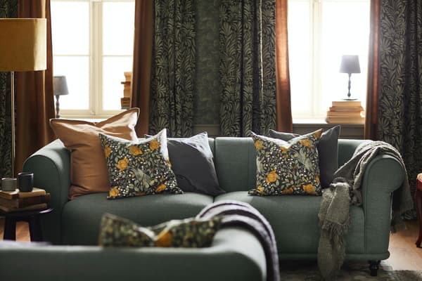 Sofa in sanften grün mit bunten und gemusterten Kissen und Decken.