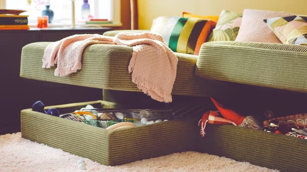 Sofa JÄTTEBO berwarna kuning-hijau gelap terbuka menunjukkan storan di dalamnya. Beberapa kusyen bercorak terletak di atasnya. Ambal berwarna putih menutupi lantai.