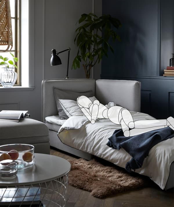 Sofa stworzona do spania w pokoju dziennym. Nałożony szkic osoby leżącej na boku, z książką leżącą na stoliku.