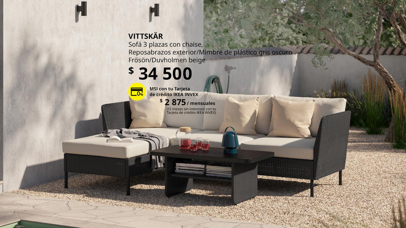 Sofá VITTSKÄR de 3 plazas para exterior con chaise longue, reposabrazos y acabado en ratán plástico color gris oscuro, con cojines FRÖSÖN/DUVHOLMEN color beige, en un espacio exterior.
